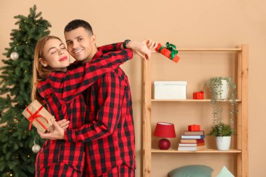 Ekose pijamalı genç bir çift Noel için dekore edilmiş oturma odasında hediyeler veriyorlar.