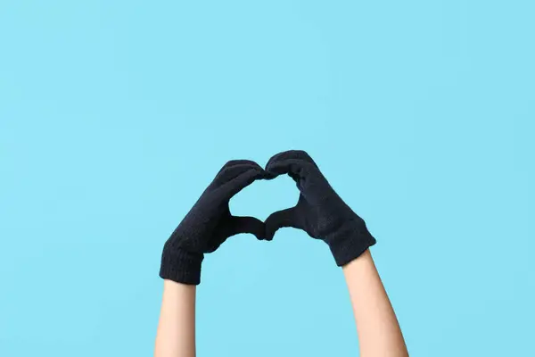 Hands in warm gloves making heart on blue background