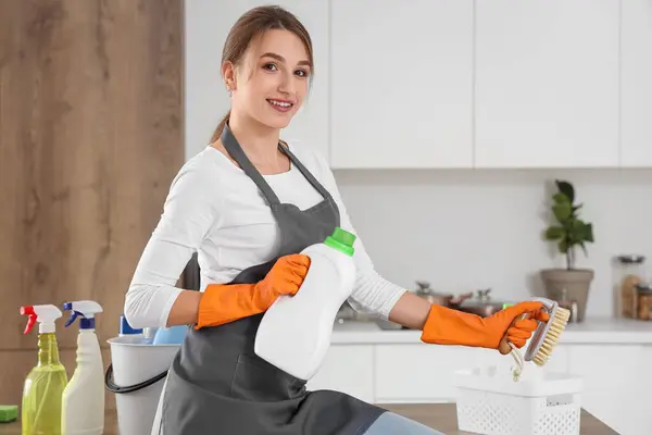 Female janitor with cleaning brush and detergent in kitchen