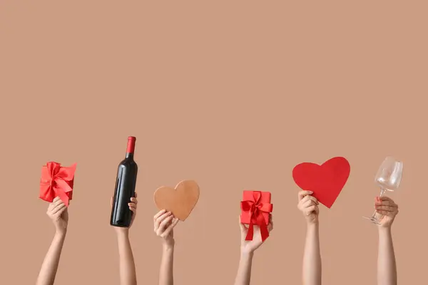 Female hands with bottle of wine, glass, gifts and decor on color background, Valentine's Day celebration