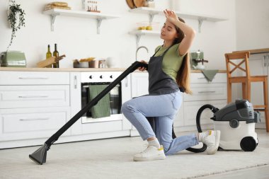 Mutfakta halı süpürmekten yorgun düşmüş genç bir kadın.
