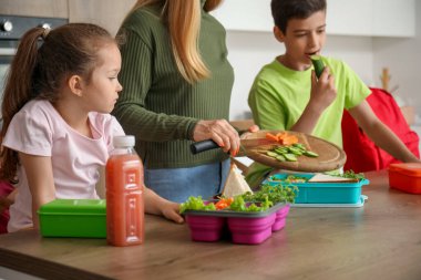 Anne, küçük çocuklarına mutfakta öğle yemeği hazırlıyor.