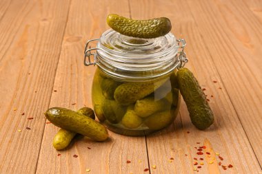 Lezzetli salatalıklı kavanoz ve ahşap arka planda baharatlar.