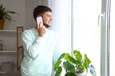 Evde cep telefonuyla konuşan genç sakallı adam.