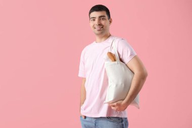 Pembe arka planda market çantalı genç adam.