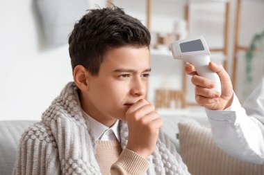 Kızıl ötesi termometresi olan bir doktor, evdeki hasta çocuğun sıcaklığını ölçüyor, yakın plan.