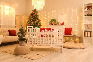 Yatak odasının içinde bebek karyolası, Noel ağaçları ve akşamları parlayan ışıklar var.