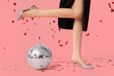 Disko topu ve kırmızı arka planda kalp şeklinde konfetileri olan güzel genç bir kadın.