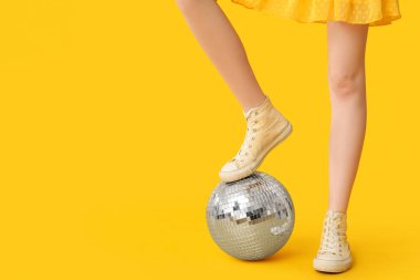 Sarı arka planda disko topu olan şık spor ayakkabılı kadın bacakları