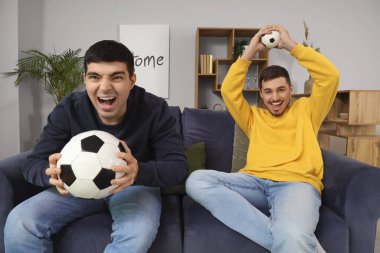Oturma odasında futbol toplarıyla kanepede oturan yakışıklı genç kardeşler.