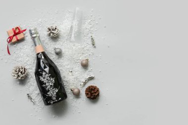 Cam kaplı bir şişe şampanya, beyaz arka planda Noel topları ve koniler.
