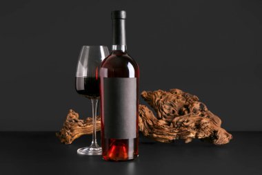 Siyah zemin üzerinde tahta olan bir şişe ve bir bardak kırmızı şarap.