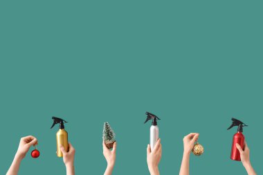 Elinde saç spreyi şişeleri ve yeşil arka planda Noel süslemeleri tutan eller.