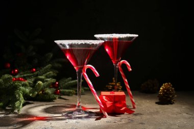 Bir bardak lezzetli kırmızı margarita, baston şekerler ve karanlık arka planda Noel dekoru.