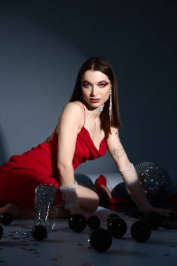 Disko topu ve bir bardak Noel süslemesi olan genç bir kadın gri arka planda oturuyor.