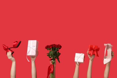 Bir buket güzel güllü kadın elleri, şık topuklu ayakkabılar ve kırmızı arka planda hediye kutuları. Sevgililer Günü kutlaması