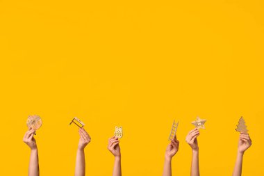 Sarı arka planda farklı Noel oyuncakları olan kadın eller.