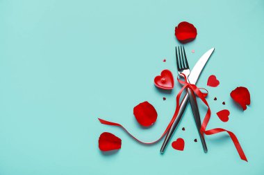 Sevgililer Günü için güzel çatal bıçak seti. Kırmızı gül yaprakları, mum ve turkuaz arka planda kalpler.