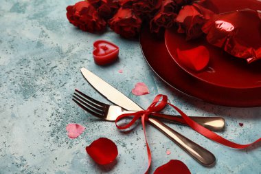 Mavi grunge arka planında kırmızı güller, mum ve dekor olan sevgililer günü için güzel bir masa.