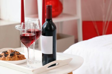 Sevgililer Günü için dekore edilmiş yatak odasındaki masada bir şişe şarap ve kruvasan.