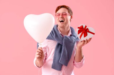 Kalp şeklinde balonu ve pembe arka planı olan genç bir adam. Sevgililer Günü kutlaması
