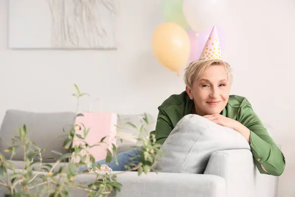 Mature woman in birthday hat sitting on sofa at home