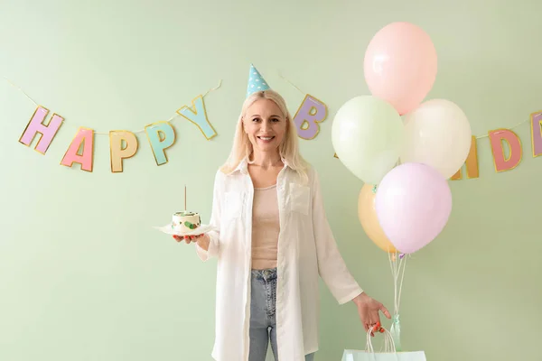 Mature woman with cake celebrating Birthday on green background