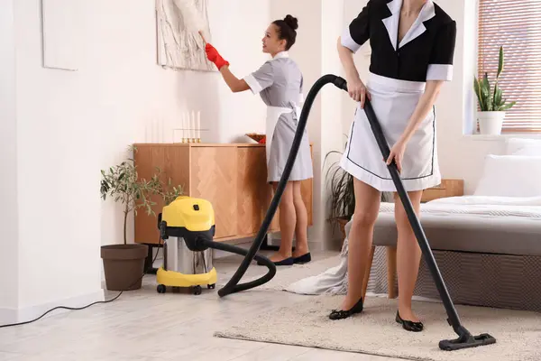 Pretty chambermaids cleaning hotel room with vacuum cleaner