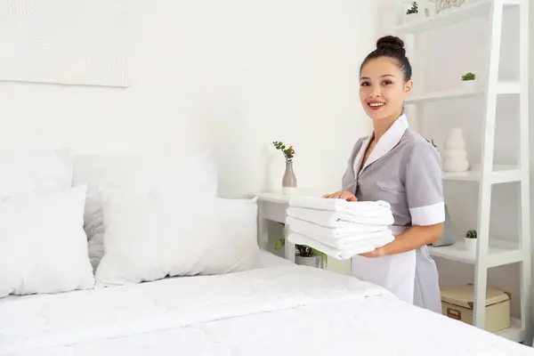 Pretty chambermaid with towels making bed in hotel room