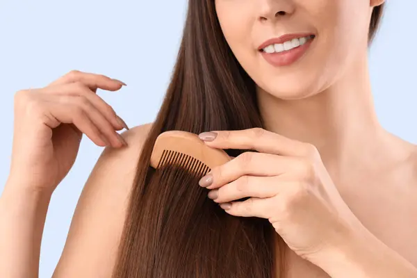 Young brunette woman combing hair on blue background, closeup