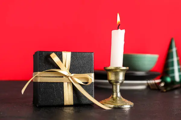Gift box with candle and decorated Christmas table setting on red background