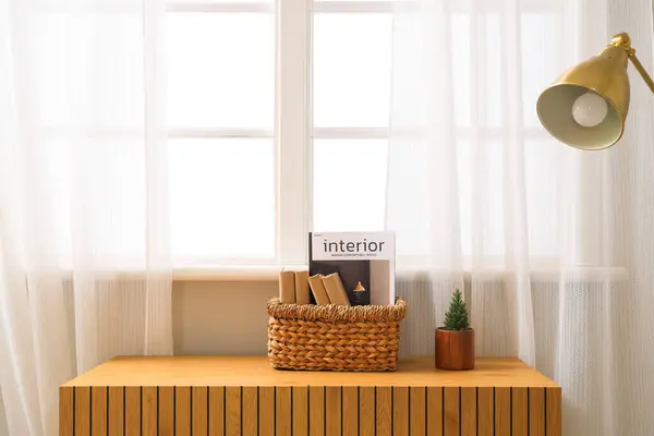 Basket with books and decorative houseplant on dresser near window