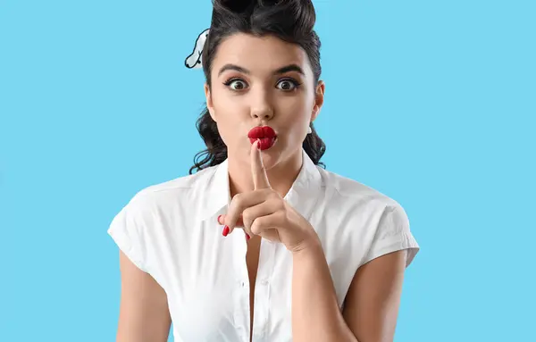 Attractive pin-up woman showing silence gesture on blue background, closeup