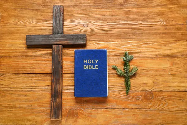 Cross with Holy Bible and fir twig on wooden background. Christmas story concept