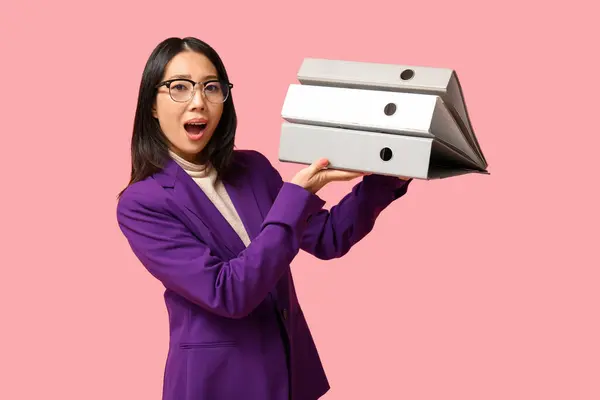 Portrait of surprised Asian businesswoman with office folders on pink background