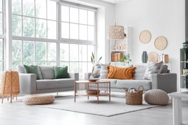 Gri koltukları, sehpası ve hasır pufları olan aydınlık oturma odasının içi.