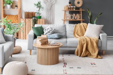 Aydınlık oturma odasının içinde şık gri kanepe ve ahşap sehpa var.