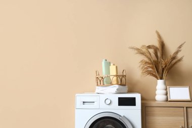 Çamaşır odasının içinde çamaşır makinesi ve ahşap dolapta otlar var.