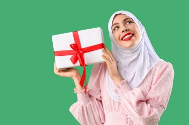 Yeşil arka planda Noel hediyesi kutusu olan güzel Müslüman kadın.