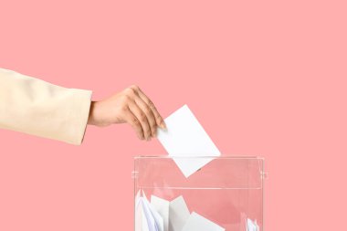 Pembe arka planda oy sandığının yanında oy veren kadın.