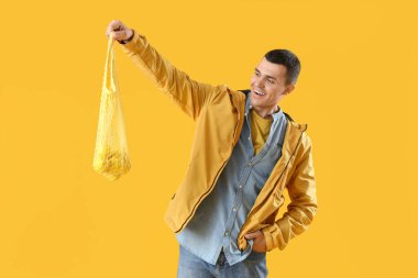 Sarı arka planda limonlu ip torbası tutan genç adam.