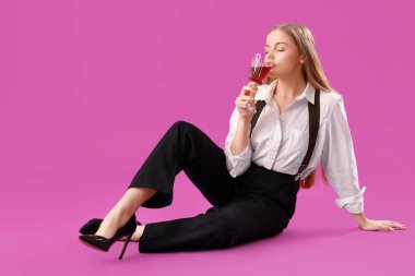 Mor arka planda şarap içen askılı şık genç bir kadın.