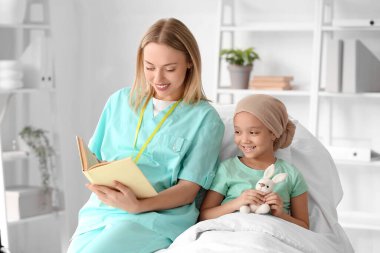 Kemoterapiden sonra küçük bir Asyalı kız ve klinikte hemşire kitabı okuyor.