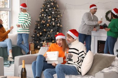 Yeni yıl partisinde erkek arkadaşının hediyesini açan genç bir kadın.