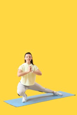 Sarı arka planda paspas üzerinde spor yapan genç bir kadın.