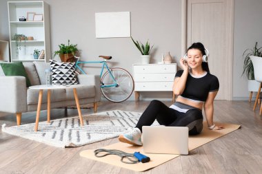 Kulaklıklı genç bir bayan evde minderde oturuyor.