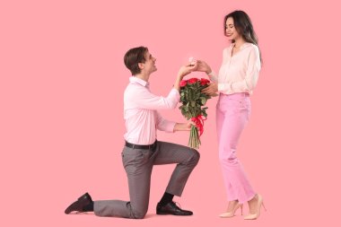 Gül ve yüzüklü genç adam pembe arka planda kız arkadaşına evlenme teklif ediyor. Sevgililer Günü kutlaması