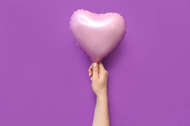 Mor arka planda kalp şeklinde hava balonu olan bir kadın eli. Sevgililer Günü kutlaması