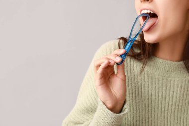 Gri arka planda dil kazıyıcısı olan genç bir kadın.