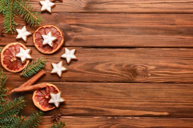Lezzetli yıldızlı kompozisyon şekilli Noel kurabiyeleri, turuncu kurumuş parçalar ve ahşap zemin üzerinde köknar ağacı dalları